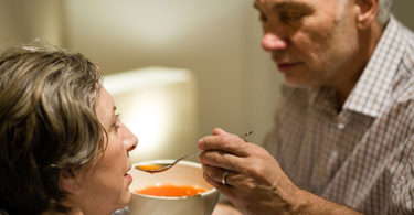 Man feeds soup to his wife, helping her to eat