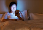 Woman in bed looking at smart phone.