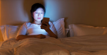 Woman in bed looking at smart phone.