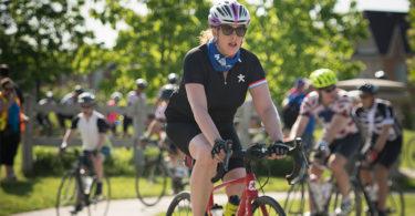 A woman wearing sunglasses and a bicycle helmet cycles towards the right-hand side of the image.