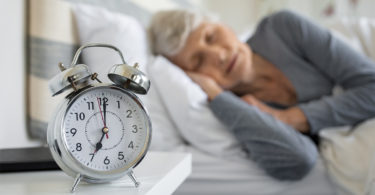 A woman sleeps behind a clock that strikes 7:00 a.m.