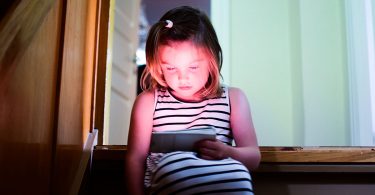 A child sitting on the stairs in the house and looking at the screens of the tablet PC, smartphone.