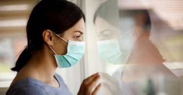 woman wearing mask and looking out window