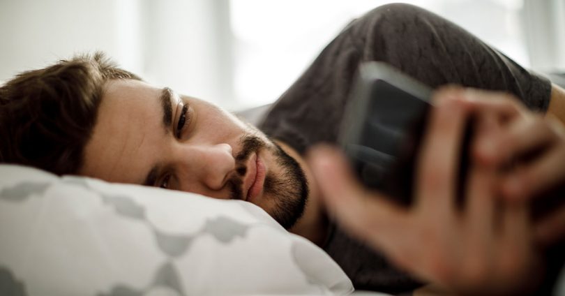 man looking sad while looking at his phone in his bed