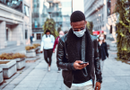 man looks at phone while walking outside with mask on