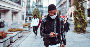 man looks at phone while walking outside with mask on