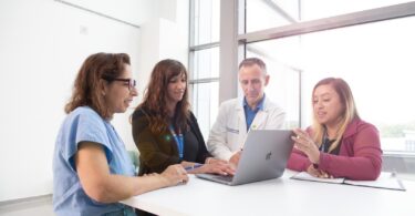 Four researchers huddled around a laptop in a well lit room