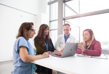 Four researchers huddled around a laptop in a well lit room