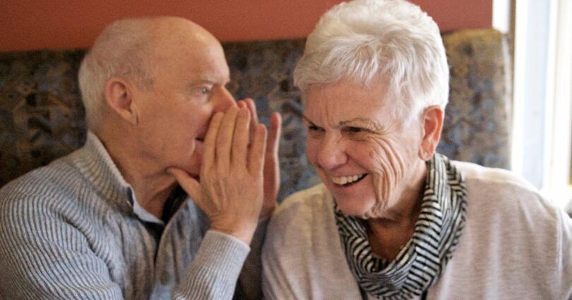 Elderly man whispers into a elderly womans ear