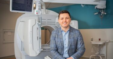 Dr. Alex Bilbily sitting in front of a CT scanner.